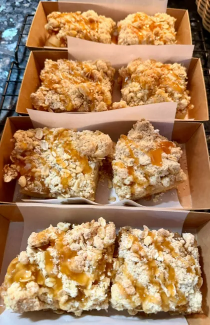 Apple crumb bars with oat crumble and caramel drizzle in paper trays