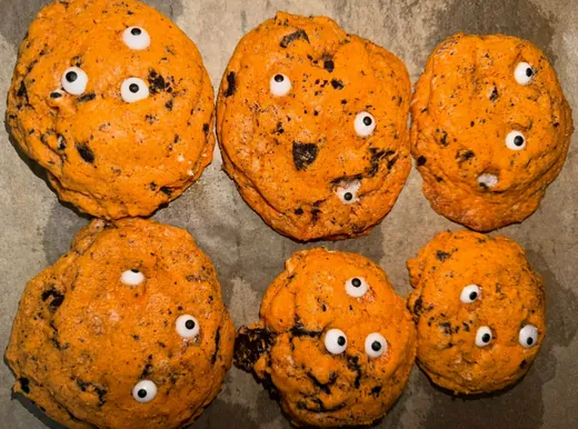 Six orange cookies studded with cookie pieces and candy eyes